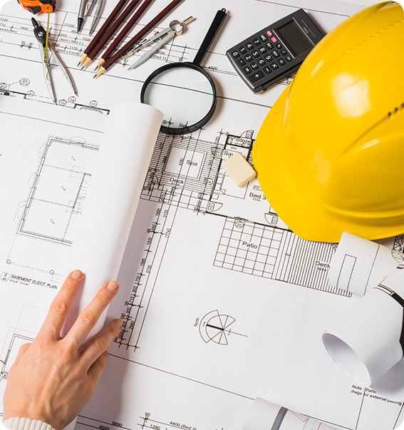 Foto com uma mão segurando um cone de folhas em cima de uma mesa eu possui um plano de construção, capacete amarelo, calculadora, lupa, borracha, lápis, compasso e trena.